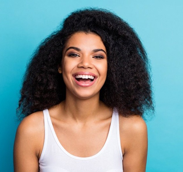 woman with dental crowns in Jacksonville smiling in front of a turquoise background