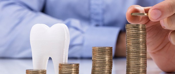 Person stacking coins next to a model of a tooth