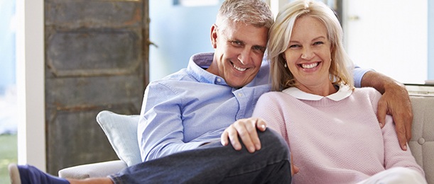 Older couple with dental implants in Jacksonville smiling on couch