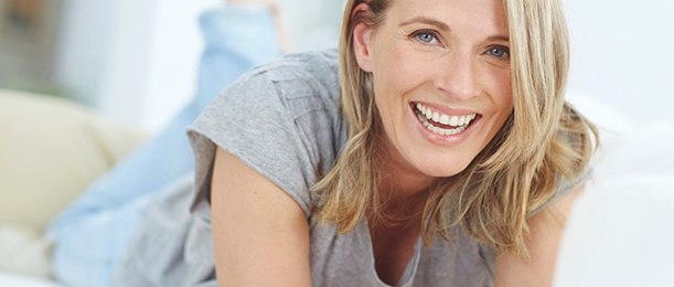 Older woman with dental implants in Jacksonville smiling on couch