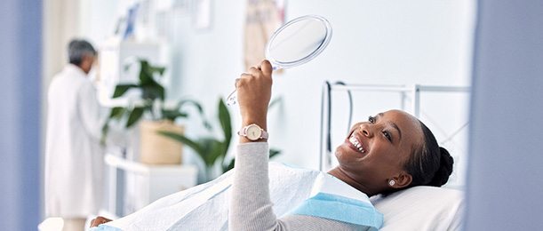 Woman smiling at reflection in handheld mirror