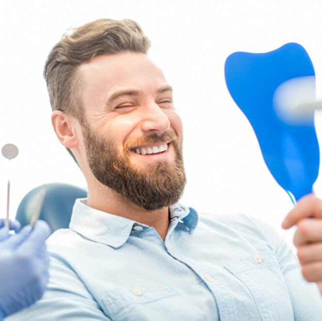 Man admiring his smile in a handheld mirror after using sedation dentistry in Jacksonville 