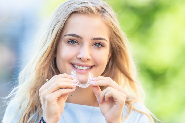 blonde woman holding invisalign aligner and smiling