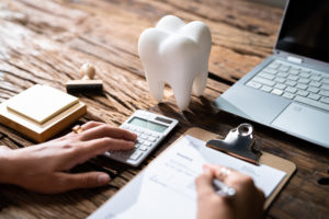 a desk with a calculator, clipboard, laptop, and model of a tooth on it