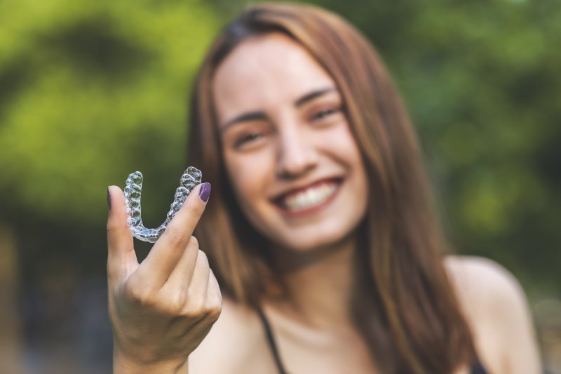 person holding Invisalign aligner and smiling