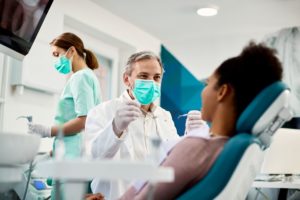 Dentist in white coat approaching patient with instruments in hands